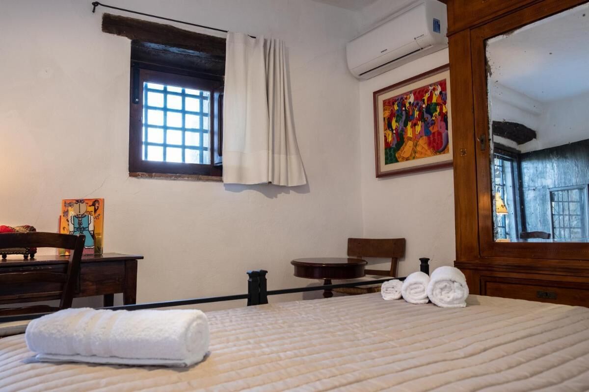 A hotel room with a bed, a window with curtains, a painting on the wall, and a wooden chair.