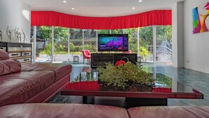 Een moderne woonkamer met een leren bank, een salontafel met een plant, een televisie op een meubel en een rood gordijn.