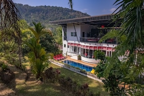 Un edificio de dos pisos con piscina, sillas rojas y un balcón.