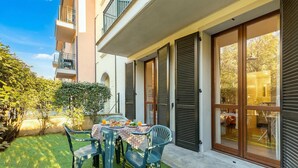 Une terrasse avec une table dressée pour deux personnes, entourée de verdure et bordée d’un bâtiment doté de grandes portes coulissantes.
