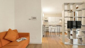 Un salon moderne avec un canapé, un téléviseur à écran plat et une cuisine en arrière-plan.
