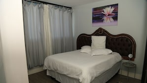 A neatly made bed with a headboard, a bedside table with a lamp, and a painting of a lotus flower on the wall. - 77 On independence Avenue (Windhoek)
