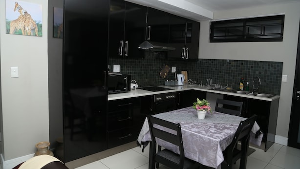 A modern kitchen with black cabinets, a tiled backsplash, a dining table with chairs, and a small potted plant. - 77 On independence Avenue (Windhoek)