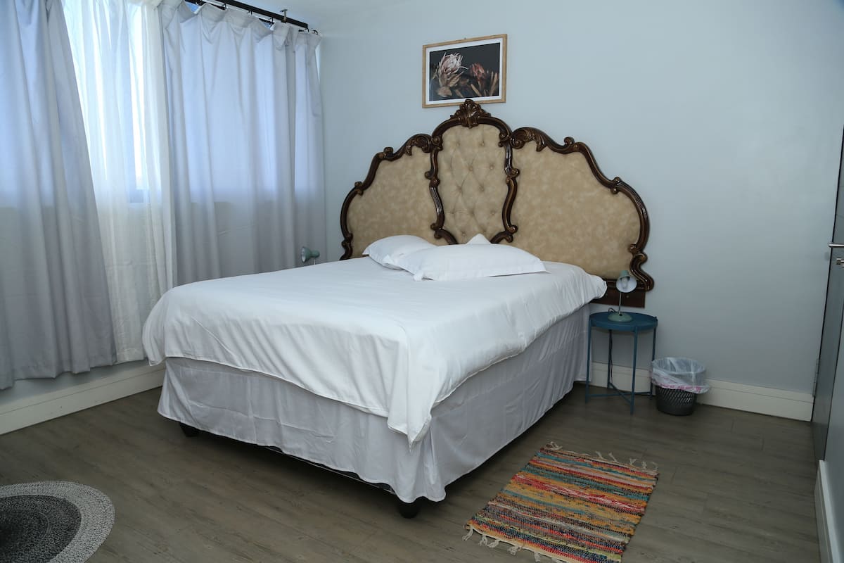 Cama bem arrumada com lençóis brancos, cabeceira de madeira e mesa de cabeceira com uma luminária.