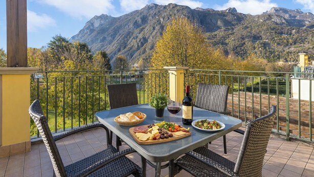 Un balcón con una mesa preparada para una comida, una botella de vino y vistas a montañas.