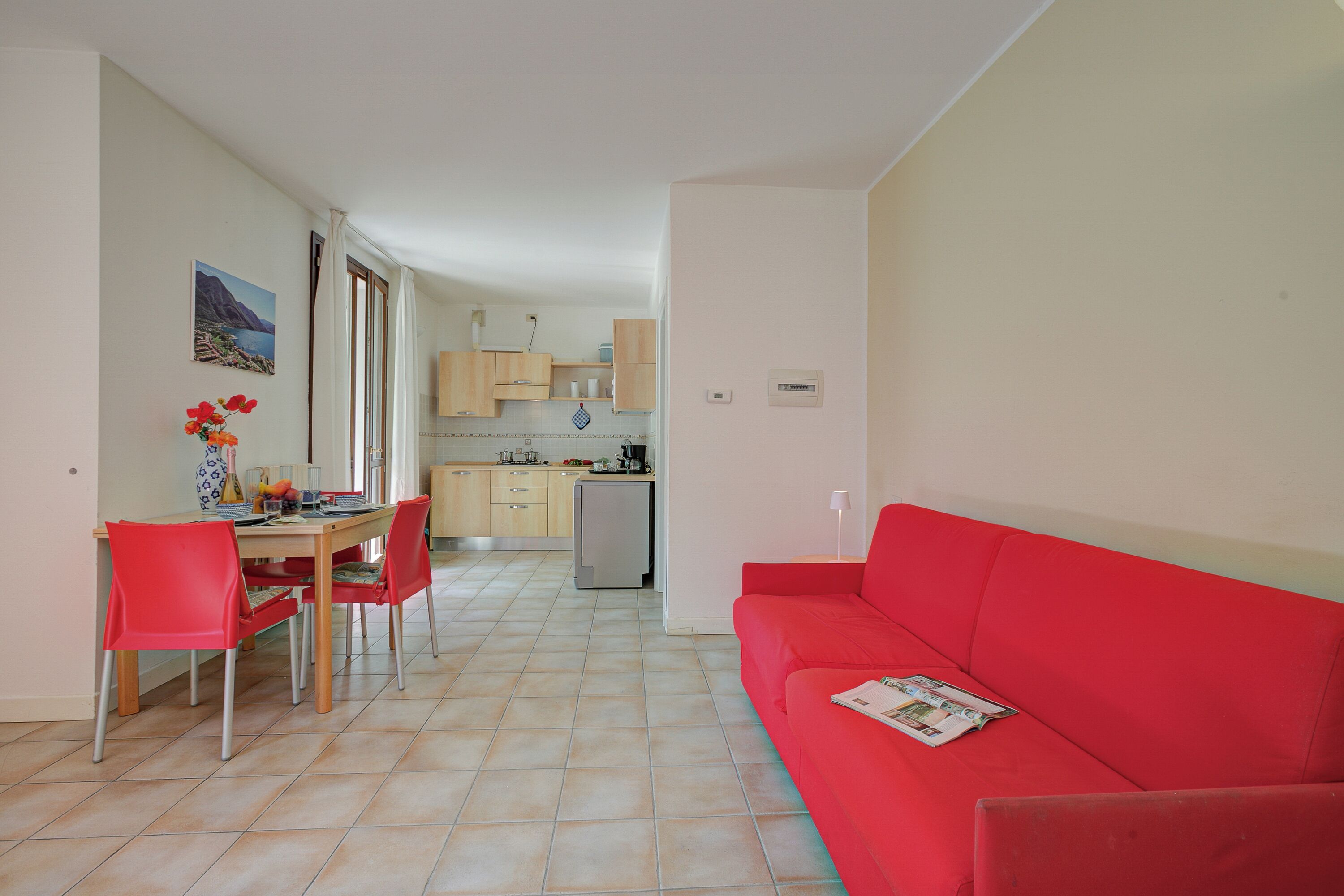 A living room with a red sofa, a dining area with a table and chairs, and a kitchen in the background.