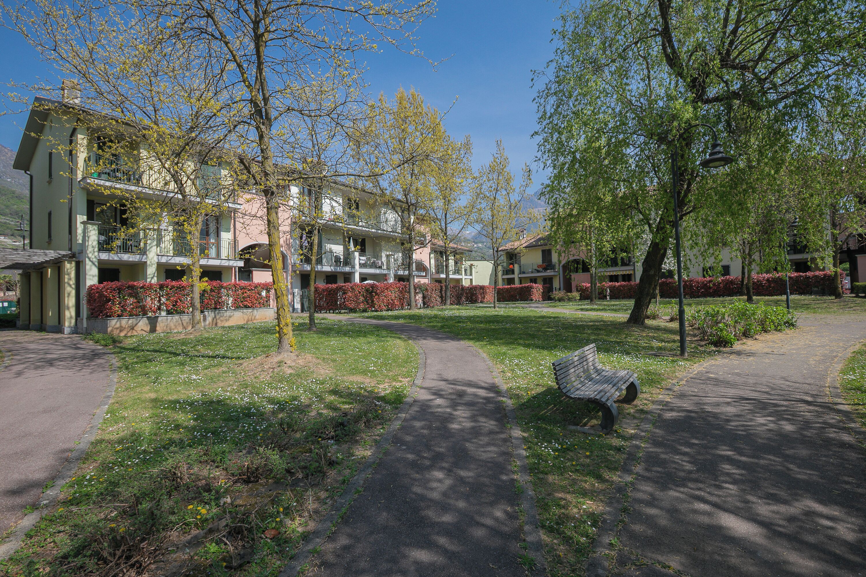 A pathway leading to a building with multiple balconies, surrounded by trees and a grassy area.