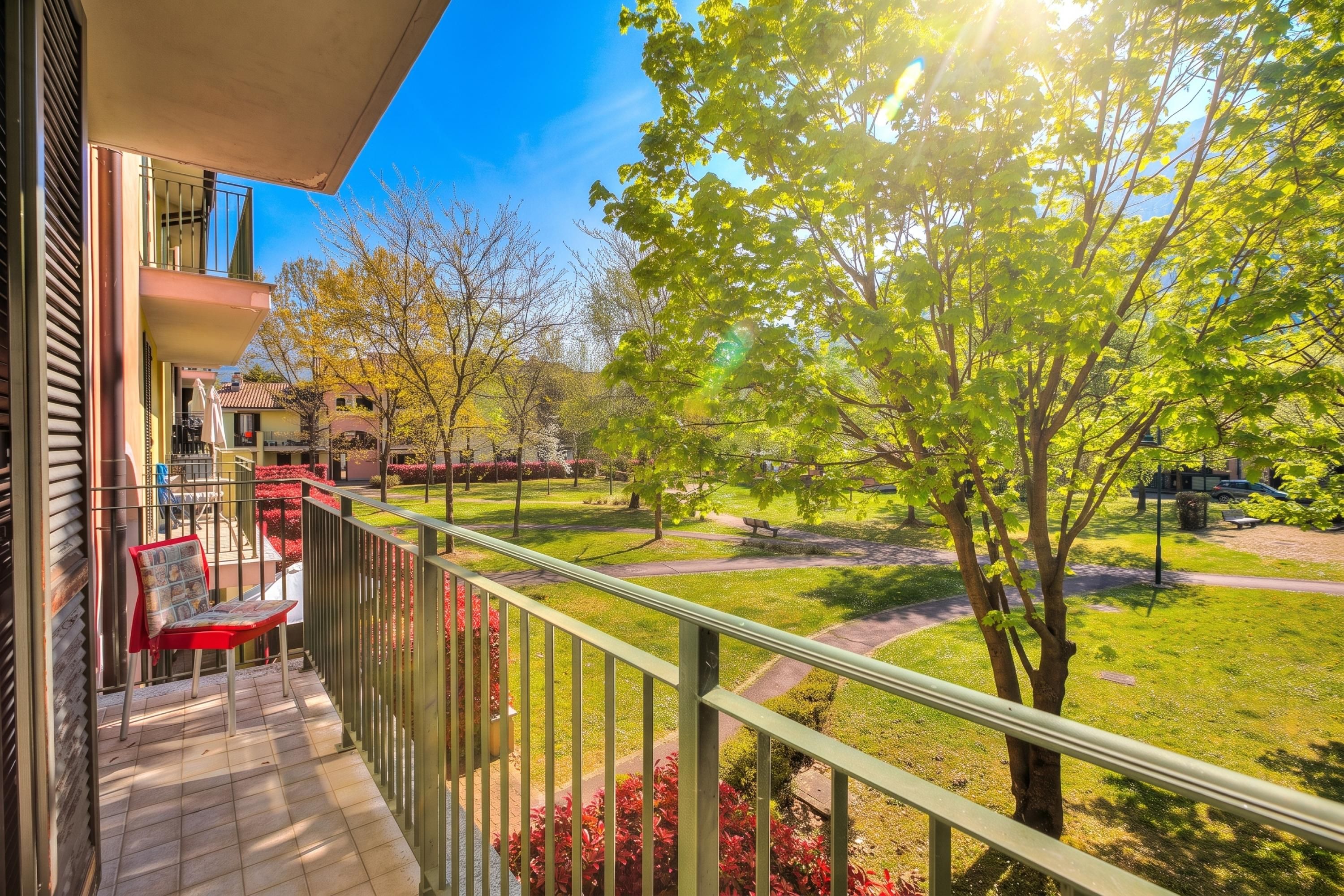 A balcony with a view of a landscaped garden and a building in the background.