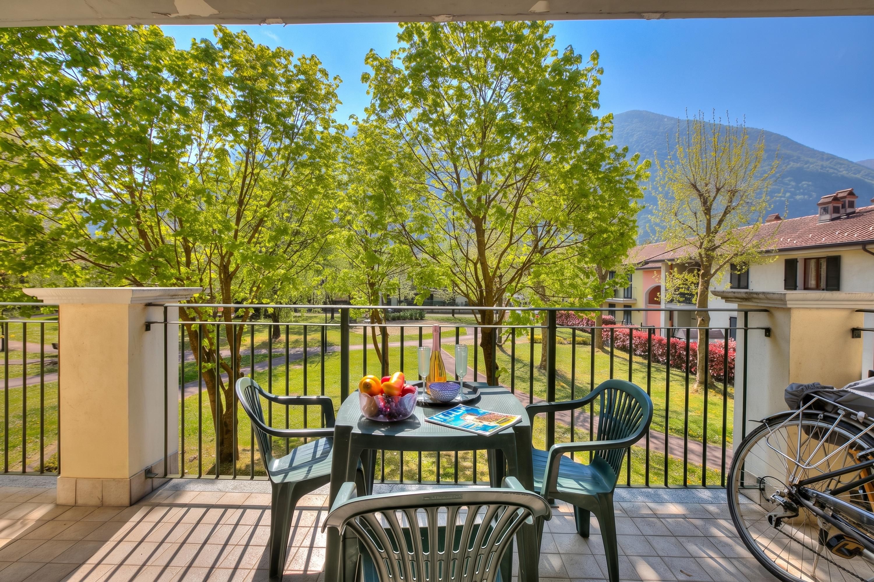 Ein Balkon mit einem Tisch für zwei Personen, Stühlen, einem Fahrrad und Blick auf einen Garten und Berge.