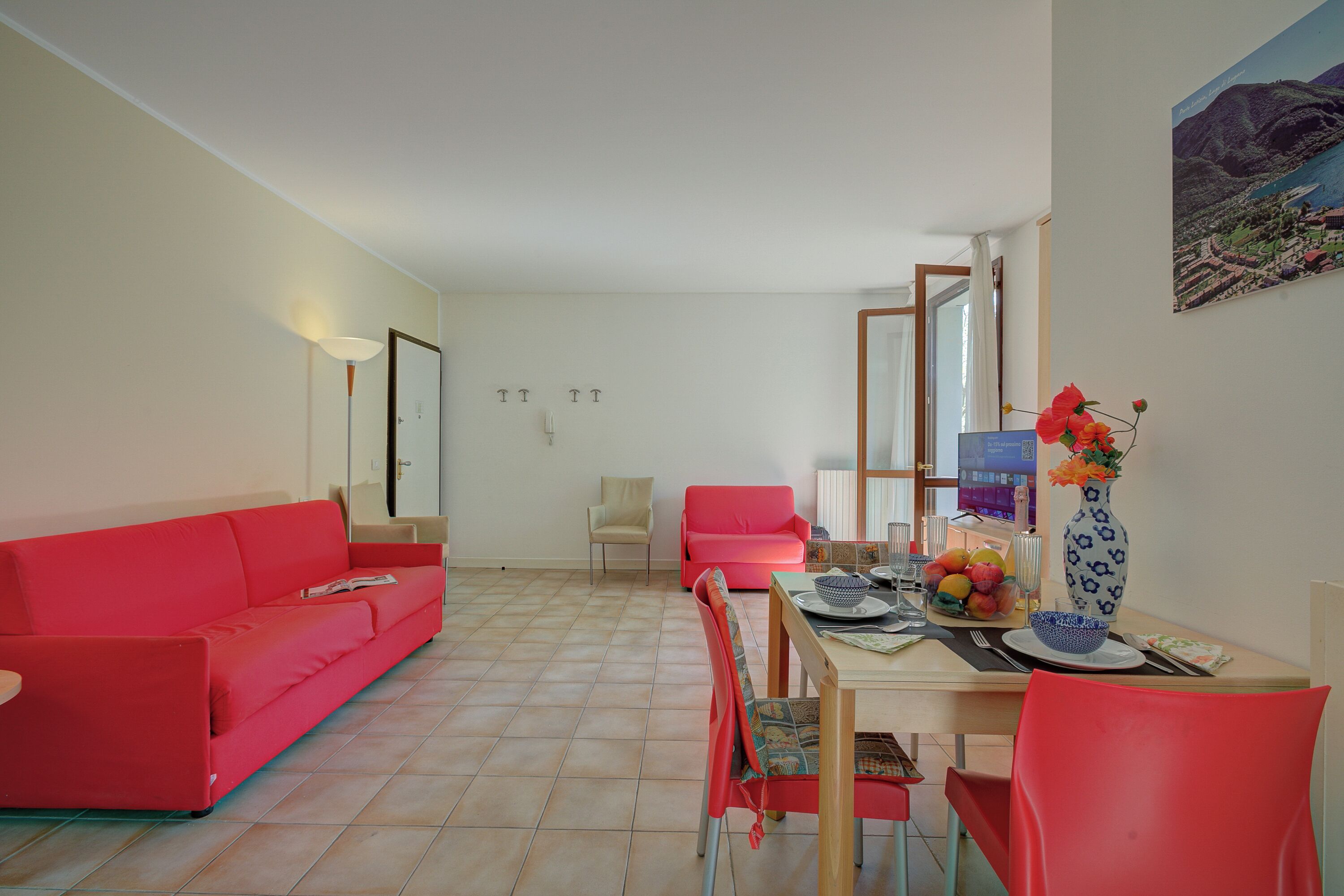 A living room with a red sofa, a dining table with chairs, and a vase with flowers.