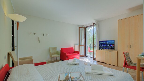 Ein Hotelzimmer mit einem Bett, einem roten Sessel, einem Fernseher und einem Holzschrank.