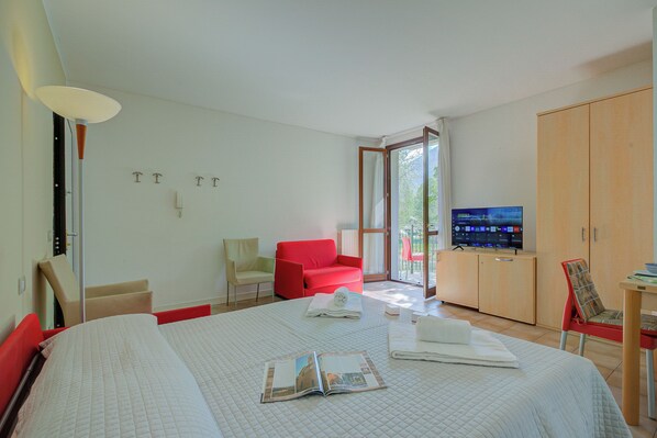 A hotel room with a bed, a red chair, a television, and a wooden wardrobe. - Porto Letizia Napoli 6, Porlezza, Italy (Porlezza)