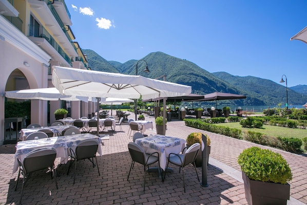 Un espace extérieur aménagé pour les repas, avec des tables, des chaises, des parasols et une vue sur les montagnes.