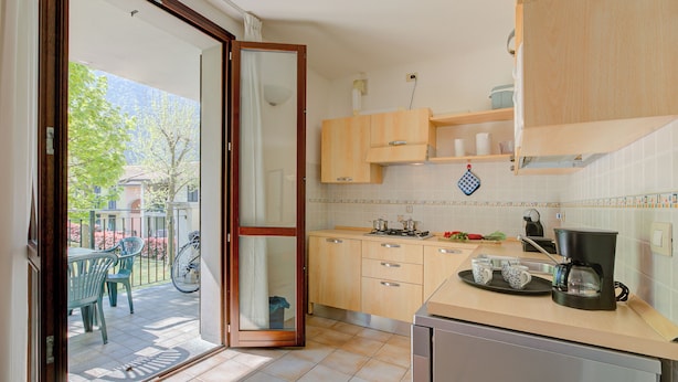 A kitchen with wooden cabinets, a coffee maker, and a dining area with chairs and a table. - Porto Letizia Napoli 6, Porlezza, Italy (Porlezza)
