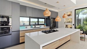 Una cocina moderna con una isla central, electrodomésticos integrados e iluminación colgante.