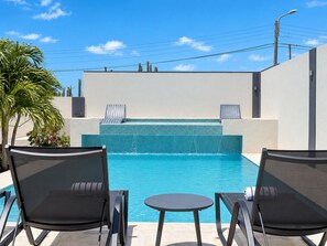 A pool area with lounge chairs and a small table, surrounded by a low wall and a palm tree.