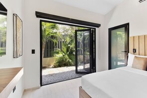 Une chambre à coucher avec un lit, une porte-fenêtre coulissante donnant sur un jardin et une tête de lit en bois.