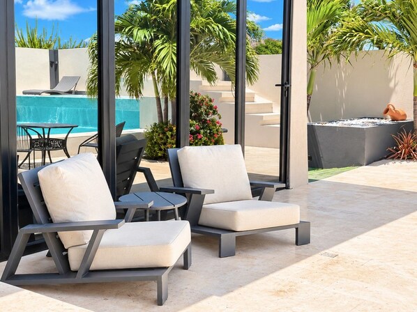 Un área junto a la piscina con dos sillas reclinables, una mesita y una fuente decorativa.