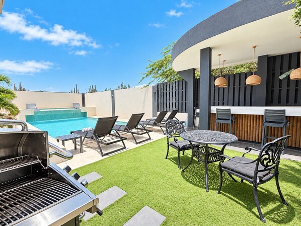 Une terrasse extérieure avec une piscine, un espace bar et un coin barbecue.