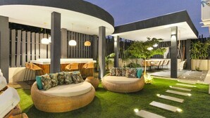 Un espacio exterior con sofás de mimbre redondos, una barra y una escalera que conduce a un porche cubierto.