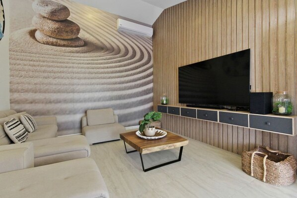 A modern living room with a large flat-screen TV, a wooden wall panel, a sofa, a coffee table, and a decorative wall feature.