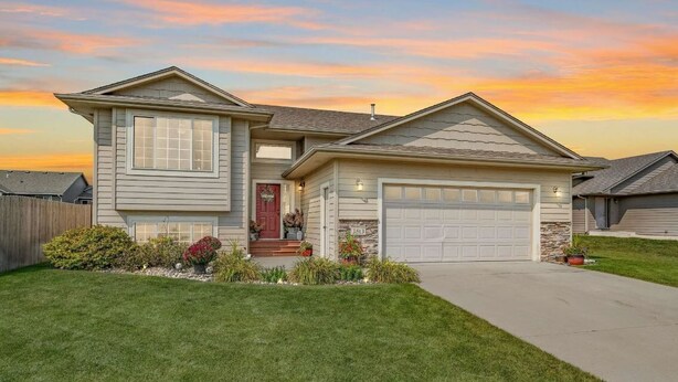 A two-story house with a garage, a front porch with a red door, and a well-maintained lawn. - East side single family home near Harmadon ball fields (Sioux Falls)