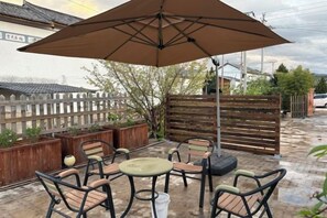 An outdoor patio with a table and chairs under a large umbrella, surrounded by wooden planters and a fence. - Shaxi Serenity Residence (Jianchuan)
