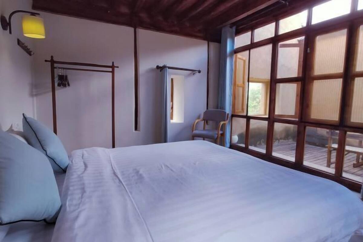 A bedroom with a bed, a chair, a window with a view, and a hanging light fixture.