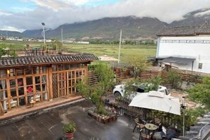 A traditional building with a tiled roof, a courtyard with seating, and a view of a mountainous landscape. - Shaxi Serenity Residence (Jianchuan)