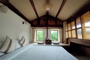 Un dormitorio con una cama grande, dos ventanas, una mesita pequeña y una lámpara colgante.