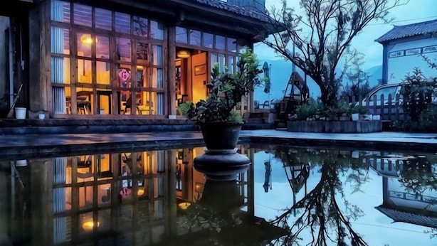 A traditional building with a reflection in the water, a potted plant, and a view of the surrounding area. - Shaxi Serenity Residence (Jianchuan)