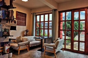 A room with a sofa, two chairs, a small table, and a bookshelf. There are large windows with a view of greenery outside. - Shaxi Serenity Residence (Jianchuan)