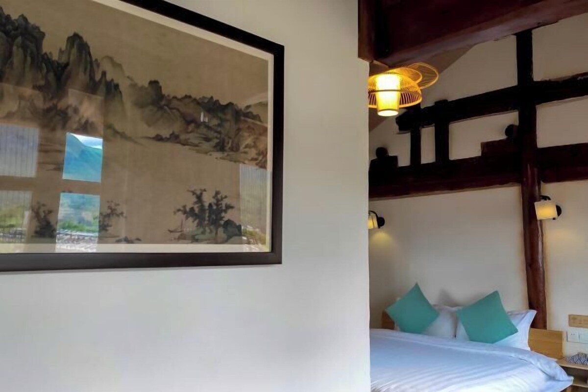 A room with a bed, a framed artwork, and a hanging light fixture.