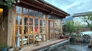 A traditional wooden building with large windows, a small outdoor seating area, and potted plants. - Shaxi Serenity Residence (Jianchuan)