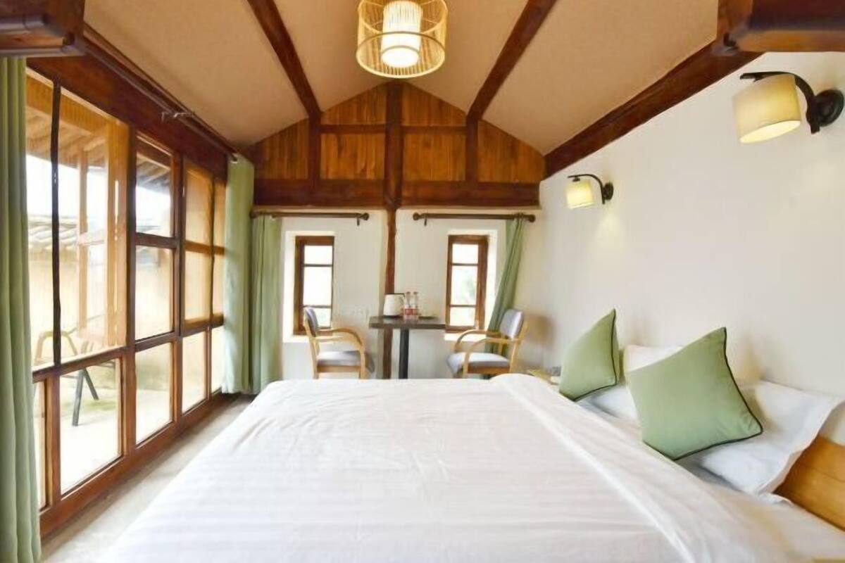 A bedroom with a large bed, two chairs, a small table, and a window with curtains.
