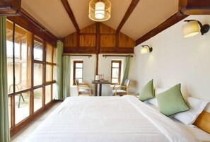 Un dormitorio con una cama grande, dos sillas, una mesita y un ventanal con cortinas.
