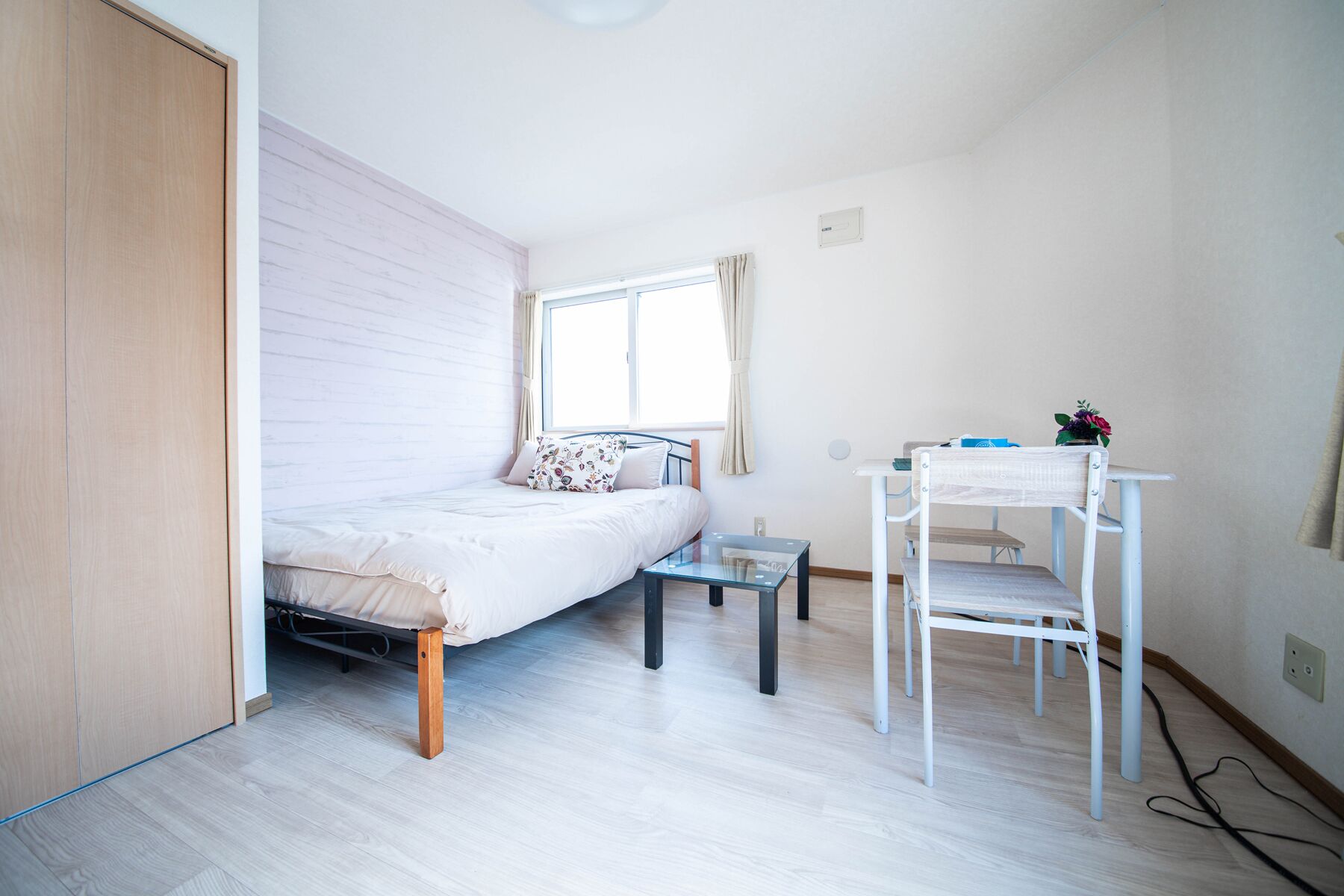 Una habitación pequeña y luminosa con una cama, una mesita y una silla.