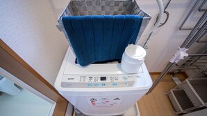 A front-loading washing machine with a digital display, a white container, and a blue towel on top. - SUMIYOSHI HOUSE ROOMB (Otaru)