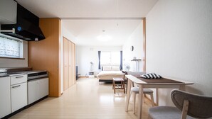 A compact hotel room with a kitchenette, a bed, a small table with chairs, and a fan. - SUMIYOSHI HOUSE ROOMB (Otaru)