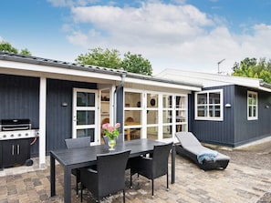 A modern outdoor dining area with a grill, wicker furniture, and a glass-enclosed patio. - 6 Person Holiday Home in Knebel (Knebel)