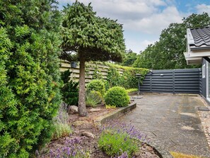 A garden with a variety of plants, a tree, and a paved area leading to a building with a tiled roof. - 6 Person Holiday Home in Knebel (Knebel)