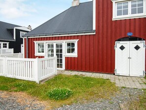 A red building with a white door and windows, a white fence, and a sign indicating a 20-minute walk.