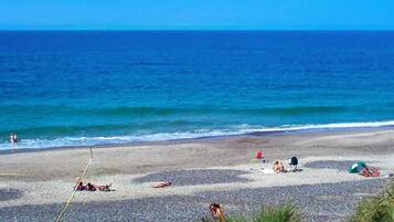 A beach with pebbles, people sunbathing, and a clear blue sky.