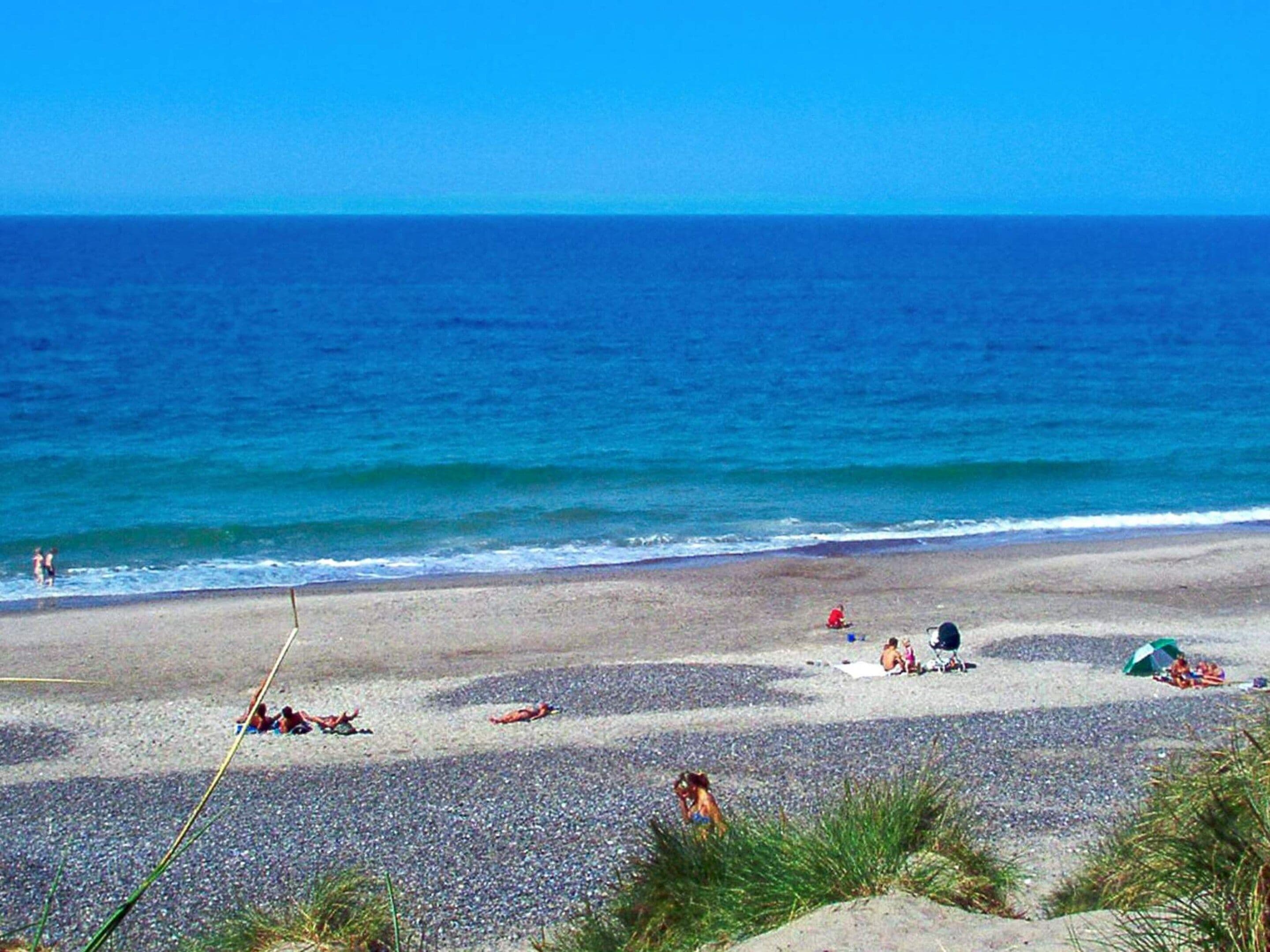A beach with pebbles, people, and a clear blue sky.