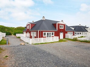 Un bâtiment rouge avec une allée gravillonnée et des clôtures blanches.
