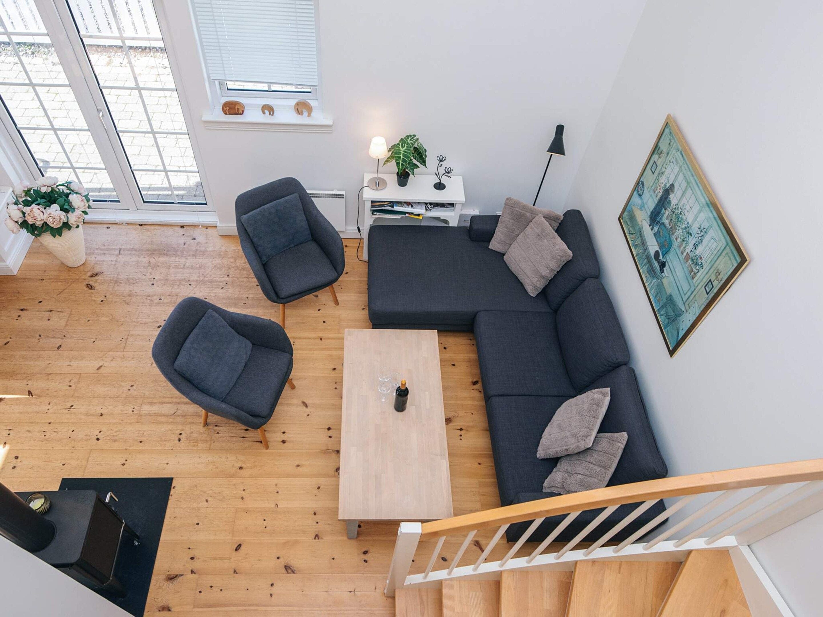 A modern living room with a sectional sofa, two armchairs, a coffee table, and a staircase.