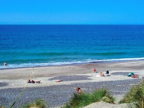 A beach with pebbles, people sunbathing, and a clear blue sky. - 4 Star Holiday Home in Ringkobing (Ringkobing)