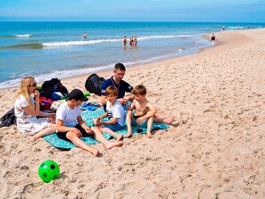 A group of people sitting on a beach towel, with a soccer ball on the sand.