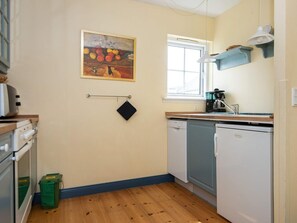 A compact kitchen with a wooden floor, a painting above the sink, and a window providing natural light. - 4 Star Holiday Home in Ringkobing (Ringkobing)