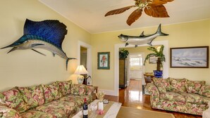 Sala de estar com sofás estampados com flores, ventilador de teto e decorações de peixes nas paredes.
